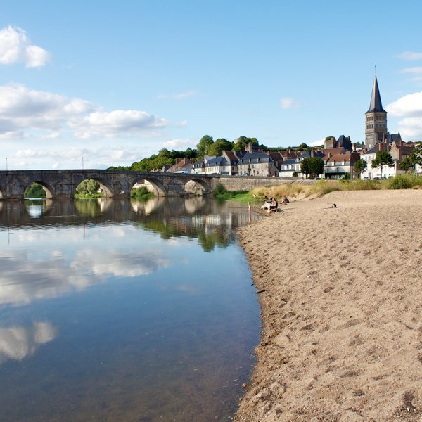 Ein ruhiger Strandabschnitt mit feinem Sand, der sanft ins Wasser übergeht, während Wolken sich im klaren Wasser spiegeln.