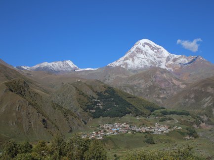Der majestätische Berg Kazbek erhebt sich über die sanften Hügel und das malerische Dorf im Tal darunter.