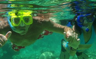 Ein Mann und eine Frau schnorcheln unter Wasser, während sie sich an den Händen halten und fröhlich in die Kamera lächeln.