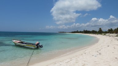 Ein kleines Boot liegt an einem ruhigen Strand, umgeben von klarem, türkisfarbenem Wasser und sanften Wellen.
