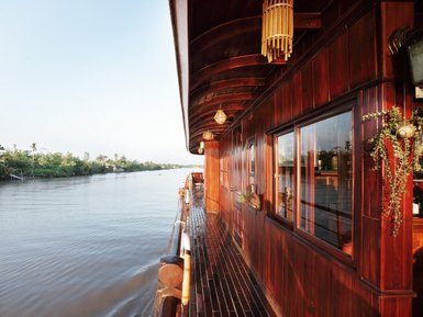 Ein elegantes Holzschiff mit einem Blick auf einen ruhigen Fluss, umgeben von üppigem Grün und klarem Himmel.