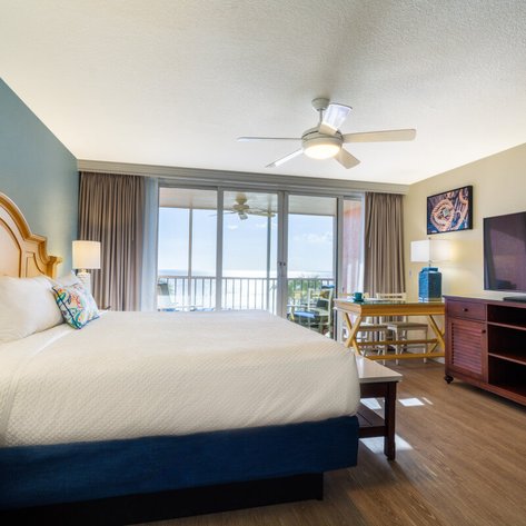 Ein helles Hotelzimmer mit einem großen Bett, einem Fernseher und einem Balkon mit Meerblick, ideal für entspannende Aufenthalte.