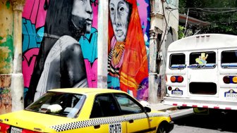 Bunte Wandmalereien zeigen Porträts von zwei Frauen und einem Mann vor einem hellgelben Taxi in einer urbanen Umgebung.