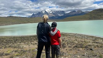 Eine Frau und ein Junge stehen am Ufer eines türkisfarbenen Sees und blicken auf die majestätischen Berge im Hintergrund.
