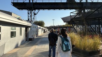 Eine Gruppe von Menschen geht auf einem gepflasterten Weg, umgeben von modernen Gebäuden und Pflanzen im Kuenstlerviertel.