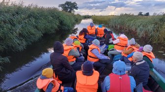 Eine Gruppe von Menschen in orangefarbenen Schwimmwesten sitzt auf einem Boot und genießt die ruhige Wasserlandschaft.