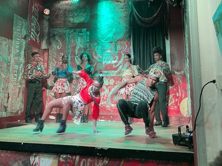 Eine lebhafte Tanzaufführung auf einer Bühne, umgeben von bunten Wänden und stimmungsvollem Licht.