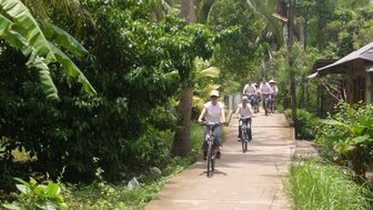 Eine Gruppe von Radfahrern fährt auf einem schmalen Weg durch die üppige Vegetation des Mekong-Deltas.