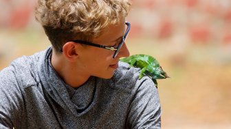 Junge trägt ein Chamäleon auf der Schulter – Tansania Reise mit Kindern