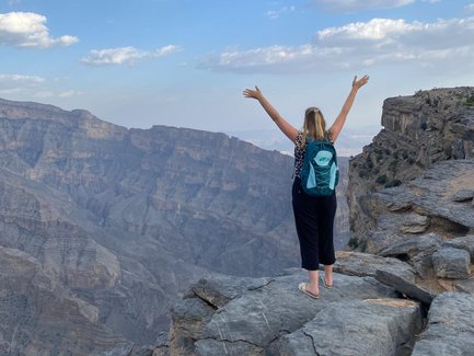Frau steht auf einem Felsen und genießt die Aussicht über die Schluchten des Jebel Shams – Oman mit Kindern
