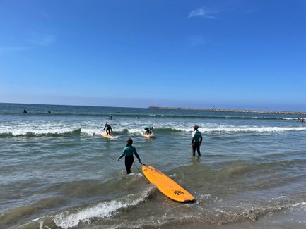 Surfer in einem Neoprenanzug geht ins Wasser, während andere auf ihren Surfbrettern warten, um die Wellen zu reiten.