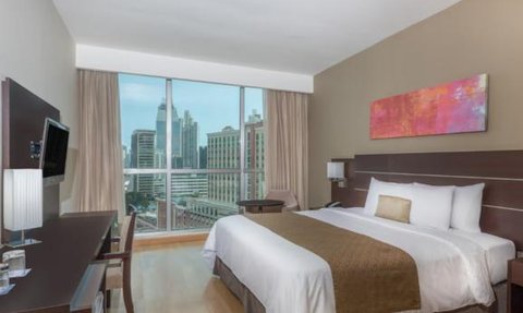 Ein modernes Hotelzimmer mit einem großen Bett, einem Schreibtisch und einem Fenster, das einen Blick auf die Stadt bietet.