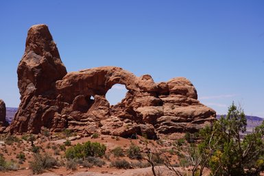 Im Arches Nationalpark erhebt sich ein beeindruckender Felsbogen aus rotem Gestein unter einem strahlend blauen Himmel.