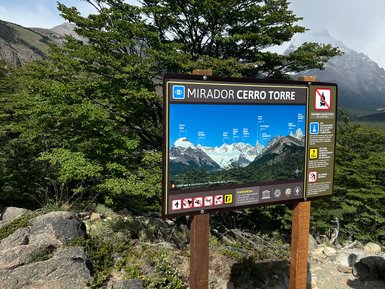 Ein Informationsschild am Mirador Cerro Torre zeigt die beeindruckende Berglandschaft mit schneebedeckten Gipfeln.