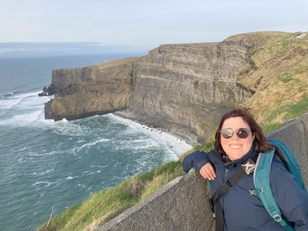 Eine lächelnde Frau mit Sonnenbrille steht an der Kante der Klippen und genießt die Aussicht auf den Ozean.