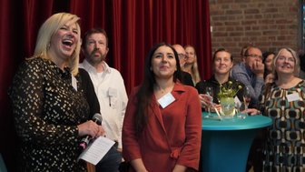 Eine Gruppe von Menschen lächelt und lacht, während sie auf eine Präsentation oder Rede aufmerksam hören.