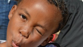 Ein fröhliches Mädchen mit geflochtenen Haaren macht eine lustige Grimasse und pustet mit einer Hand in die Luft.