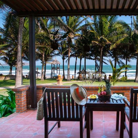 Ein einladender Veranda-Bereich mit Blick auf das Meer, umgeben von Palmen und einer entspannten Atmosphäre.