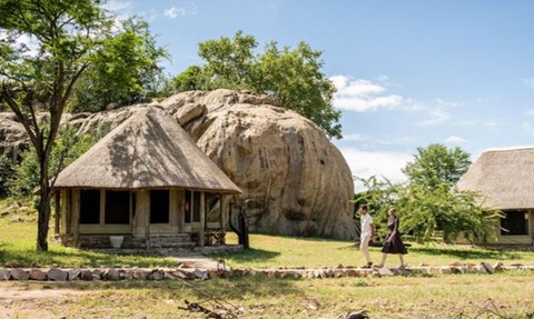 Zwei Personen spazieren auf einem Pfad zwischen zwei traditionellen Hütten in einer malerischen Landschaft.