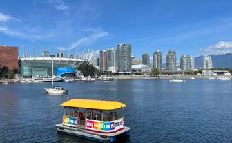Ein buntes Aquabus-Boot fährt auf dem ruhigen Wasser vor der beeindruckenden Skyline von Vancouver.