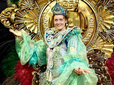 Eine festlich gekleidete Person strahlt Freude aus, gekleidet in einem glitzernden grünen Kostüm mit prachtvollen Verzierungen.