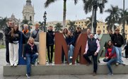 Eine Gruppe von Menschen posiert fröhlich vor dem großen, bunten Schriftzug 'LIMA' in einer Stadtlandschaft.