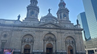 Die beeindruckende Fassade einer Kathedrale mit zwei Türmen und Statuen, umgeben von Menschen und modernen Gebäuden.