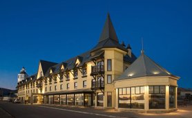 Ein elegantes Hotel mit spitzen Türmen und großen Fenstern, das in der Dämmerung beleuchtet ist.