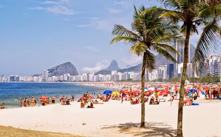 Ein sonniger Strand von Copacabana mit vielen Menschen, farbigen Sonnenschirmen und einer tollen Kulisse von Gebäuden.