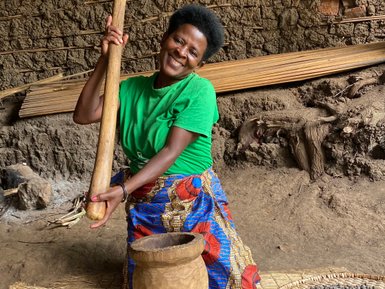 Eine fröhliche Frau in einem grünen T-Shirt mahlt mit einem Holzstößel in einem traditionellen Mörser aus Holz.