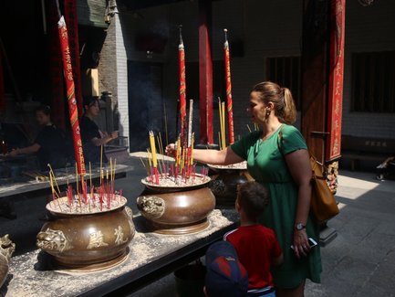Eine Frau in einem grünen Kleid zündet Räucherstäbchen in einem Tempel an, während ein Kind aufmerksam zuschaut.