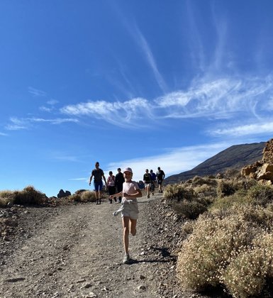 Ein Mädchen in einem weißen T-Shirt und Shorts läuft fröhlich auf einem Wanderweg, umgeben von einer Gruppe von Menschen.
