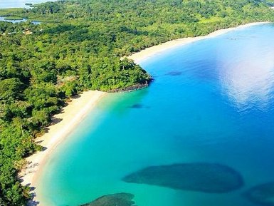 Ein atemberaubender Blick auf einen ruhigen Strand mit klarem, türkisfarbenem Wasser und üppiger grüner Vegetation im Hintergrund.