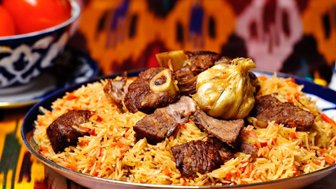 Ein Teller mit duftendem Plov, der mit zartem Fleisch und aromatischem Reis garniert ist, vor einem bunten Hintergrund.