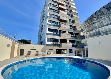 Ein blauer Pool reflektiert den klaren Himmel, umgeben von einem modernen Apartmentgebäude mit Balkonen.