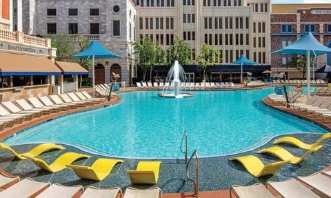 Ein einladender Pool mit klarem Wasser, umgeben von gelben Liegen und schattenspendenden Sonnenschirmen in einer urbanen Umgebung.