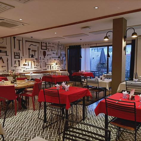Ein stilvolles Restaurant mit roten Tischdecken, Holzstühlen und einer kreativen Wanddekoration aus Werkzeugen.