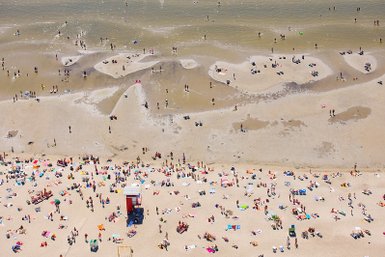Ein belebter Strand mit vielen Menschen, die sich auf Handtüchern entspannen und im Wasser spielen.