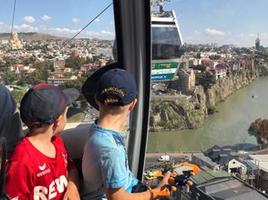 Zwei Jungen in einer Seilbahn blicken auf die Stadt und den Fluss, während sie die Aussicht genießen.