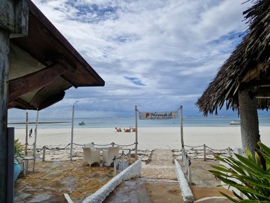 Ein Blick auf den Strand mit einem Schild, das das Nomad Beach Bar & Restaurant anzeigt, umgeben von sanften Wellen.