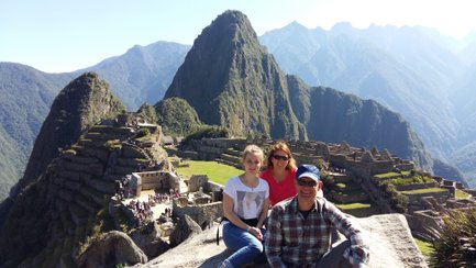 Drei Personen posieren fröhlich vor der beeindruckenden Kulisse von Machu Picchu, umgeben von majestätischen Bergen.