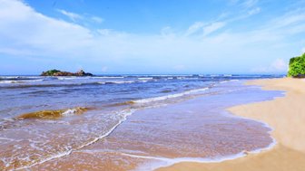Ein ruhiger Strand mit sanften Wellen, die an den goldenen Sand spülen, unter einem strahlend blauen Himmel.