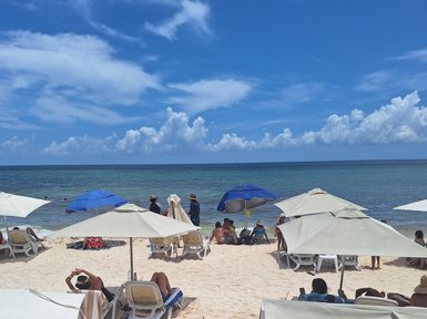Am Strand von Playa del Carmen entspannen Menschen unter Sonnenschirmen, während die Wellen sanft ans Ufer plätschern.