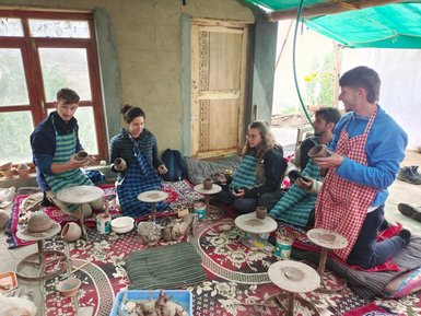 Fünf Personen sitzen in einem Töpferatelier, konzentriert auf ihre Töpferarbeiten, umgeben von Töpfermaterialien und Werkzeugen.