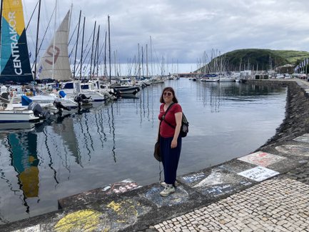 Eine Frau steht am Hafen, umgeben von Booten und Yachten, während sich die Wolken über dem Wasser spiegeln.