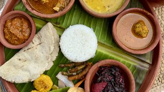 Ein traditionelles indisches Essen auf einem Teller aus Ton, serviert mit Reis, verschiedenen Currys und frischem Gemüse.