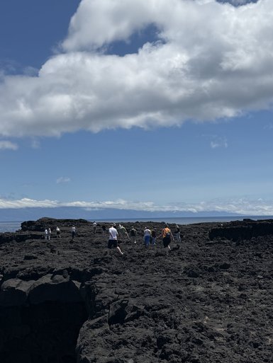 Eine Gruppe von Menschen erkundet eine vulkanische Landschaft mit schwarzem Lavagestein unter einem strahlend blauen Himmel.