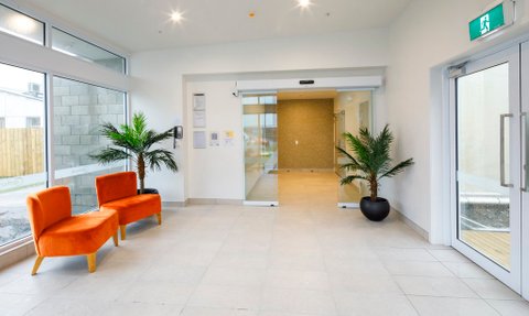 Der Empfangsbereich des Greymouth Copthorne Hotels zeigt moderne, orangefarbene Stühle und eine grüne Pflanze in einem hellen Raum.