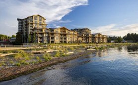 Ein modernes Resort am Wasser, umgeben von üppigem Grün und einem klaren Himmel, ideal für entspannende Urlaube.