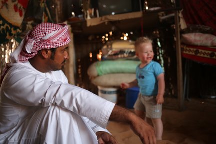 Ein Omani sitzt mit einem Kleinkind in traditioneller Kleidung – Oman Reise mit Kindern